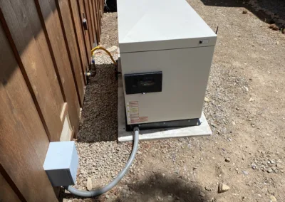 Outdoor electrical equipment with a conduit running into a ground-mounted box next to a wooden fence.