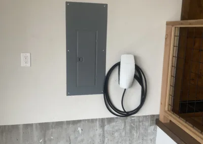 An electric vehicle charging station mounted on a garage wall next to an electrical panel.