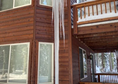 A wooden cabin with prominent icicles hanging from the roof on a snowy day.